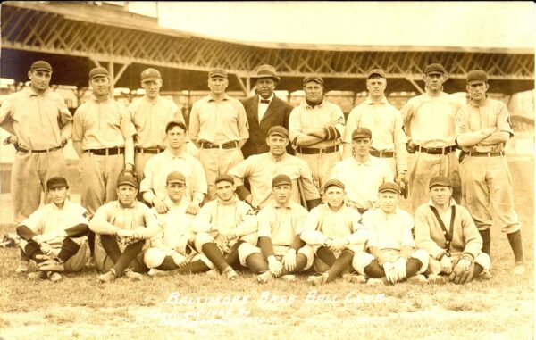 Postcard showing baseball players seated and standing in stadium.